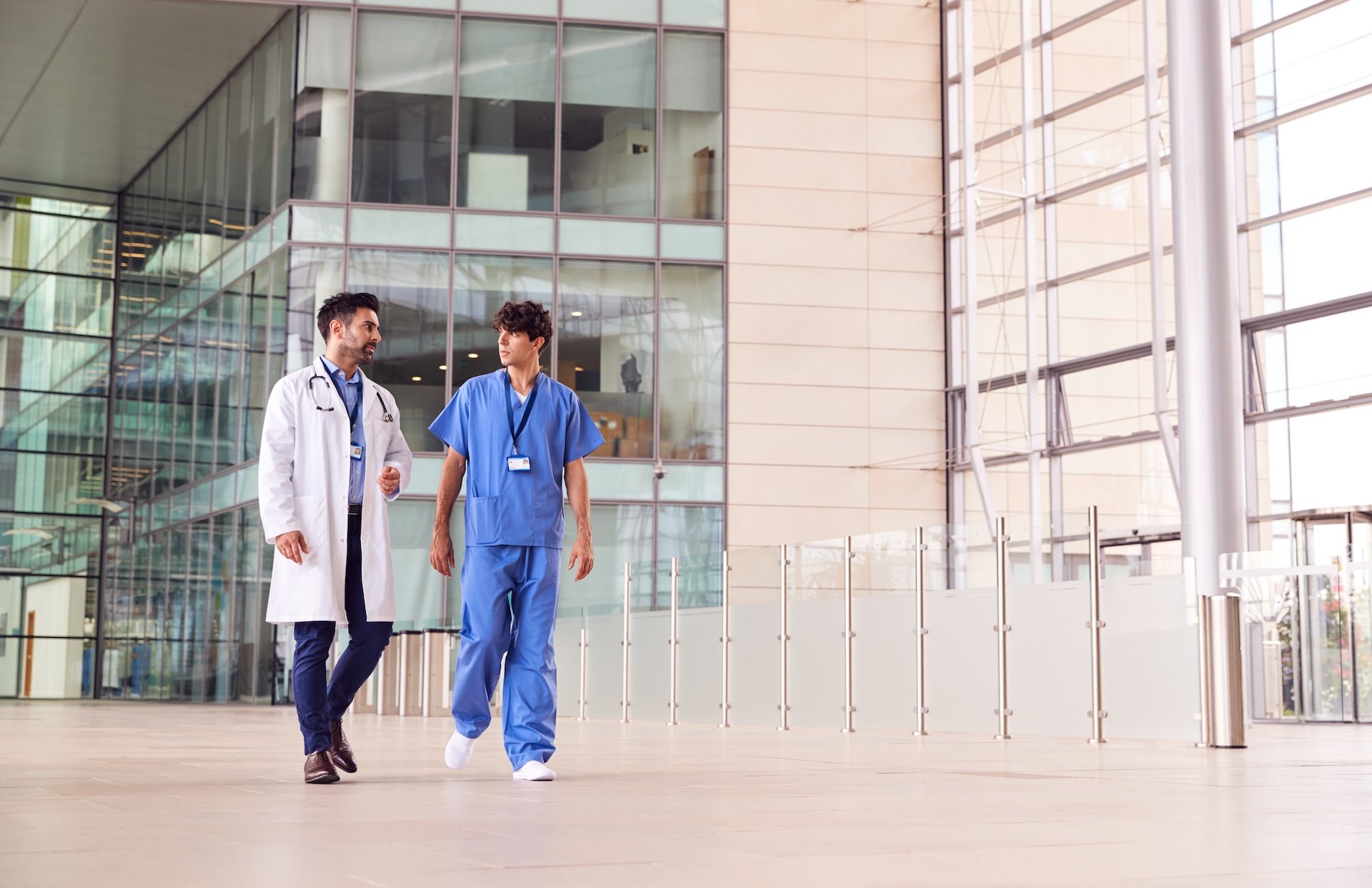 male-medical-staff-talking-as-they-walk-through-lo-2026-03-10-03-16-31-utc